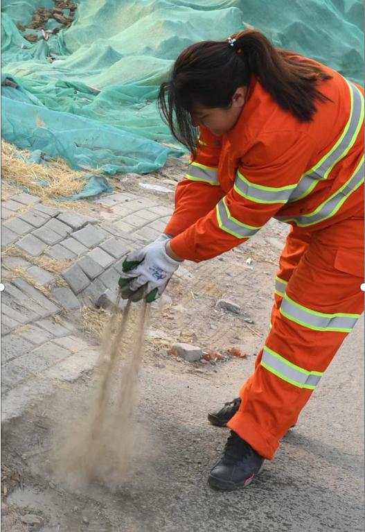 图为李萌用沙土掩盖抽粪车作业时洒漏在街边的粪水,以减少气味